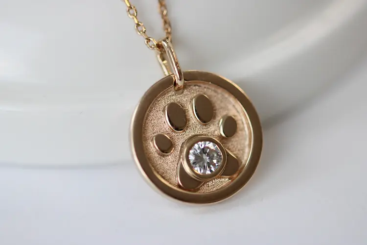 A circle shaped pendant with a dog paw print and colorless memorial diamond in the middle