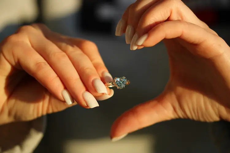 A woman making half a heart with one hand, holding a heart shaped blue memorial diamond ring in the other