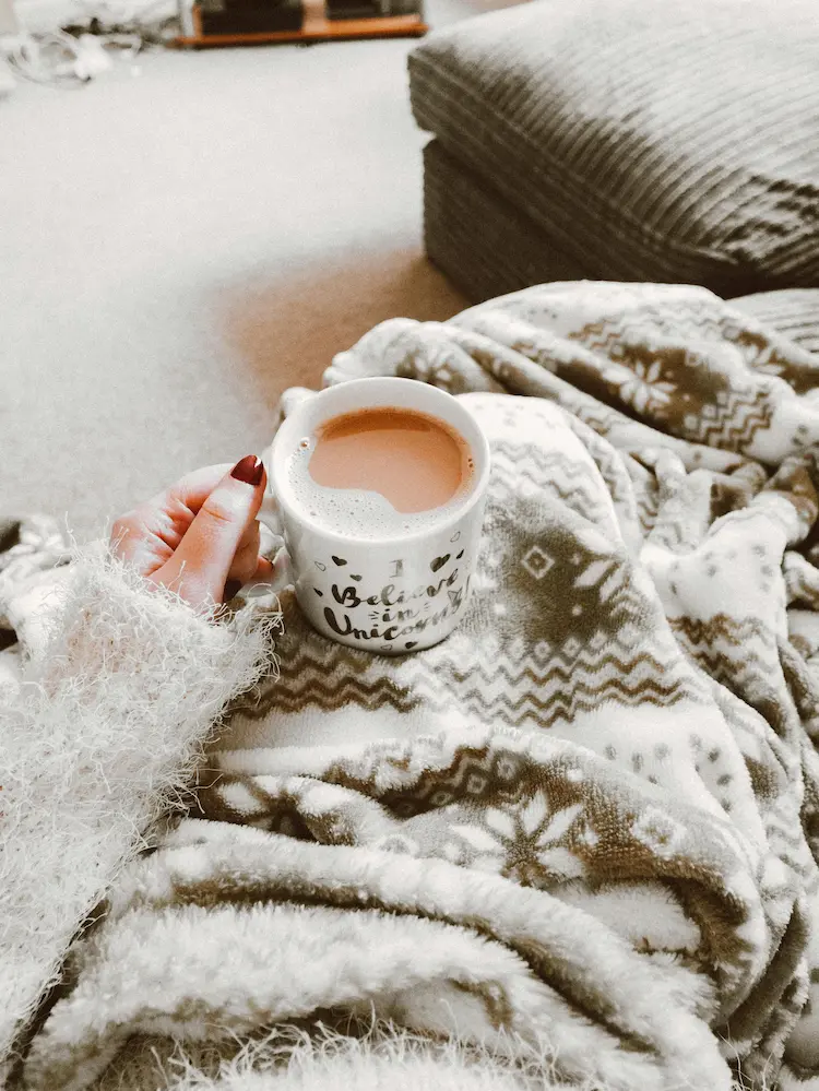 Cozy blanket, person holding a cup pf hot chocolate over it