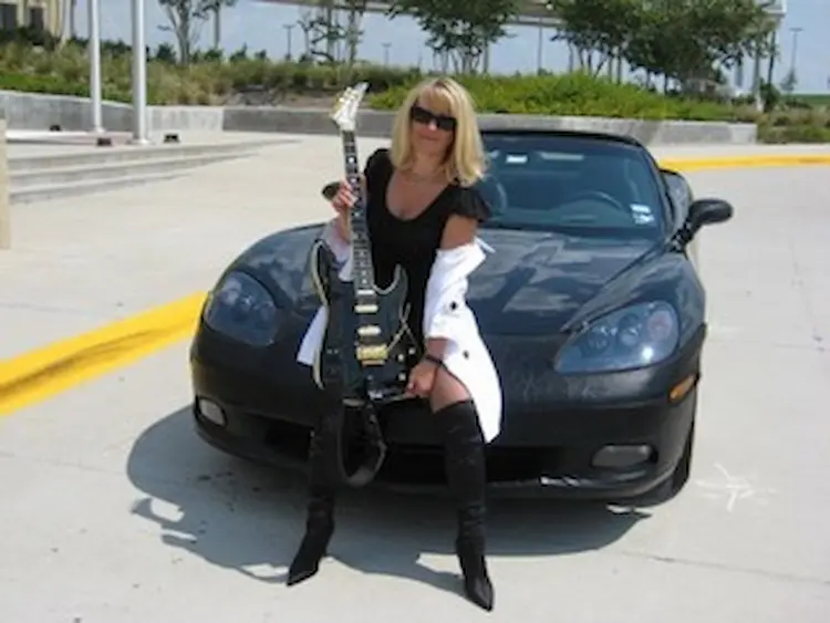 A stunning blonde woman sitting on a Porsche with an electric guitar in her hands