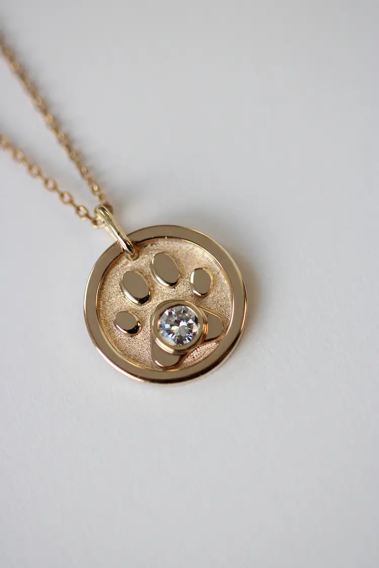 A round pendant with a paw design and memorial diamond in the middle of it