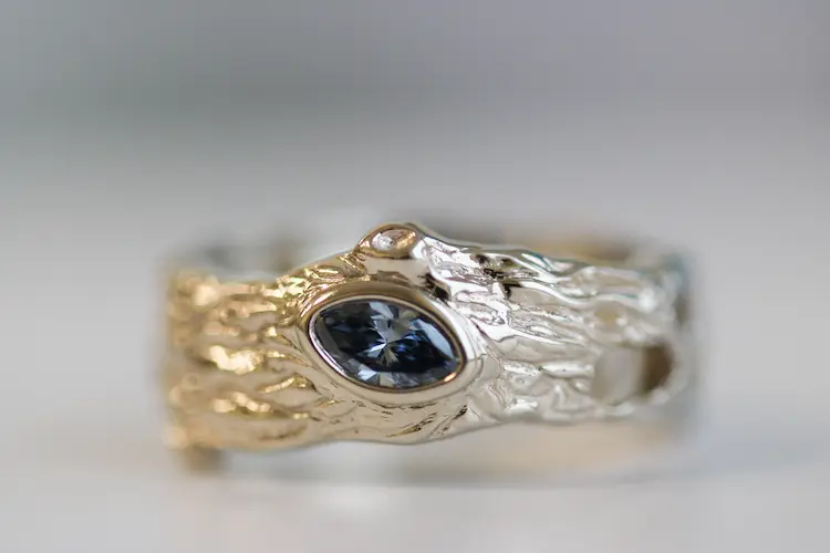 A blue marquise memorial diamond, set in a ring that resembles tree bark.