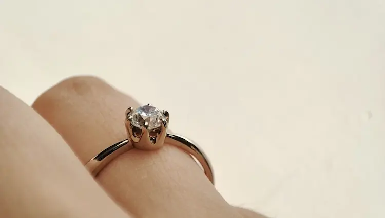 A colorless memorial diamond set in a gold ring, on a finger.