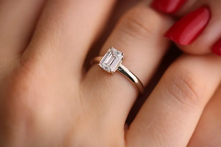 A colorless emerald cut memorial diamond set in a ring, on a finger.
